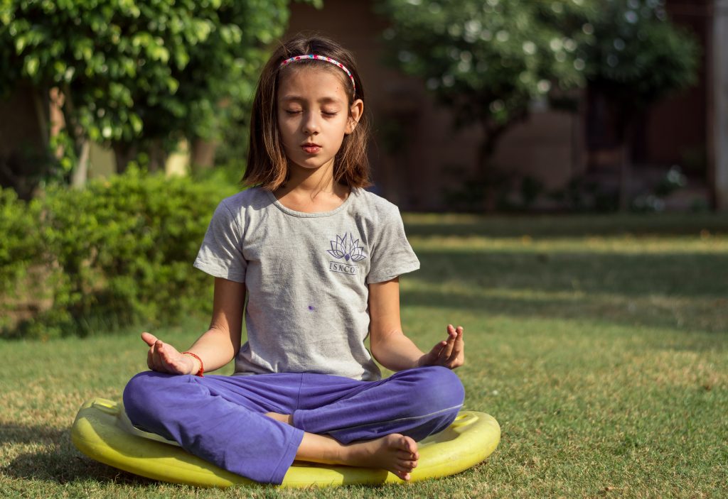 girl performing meditation on yellow seat outdoors